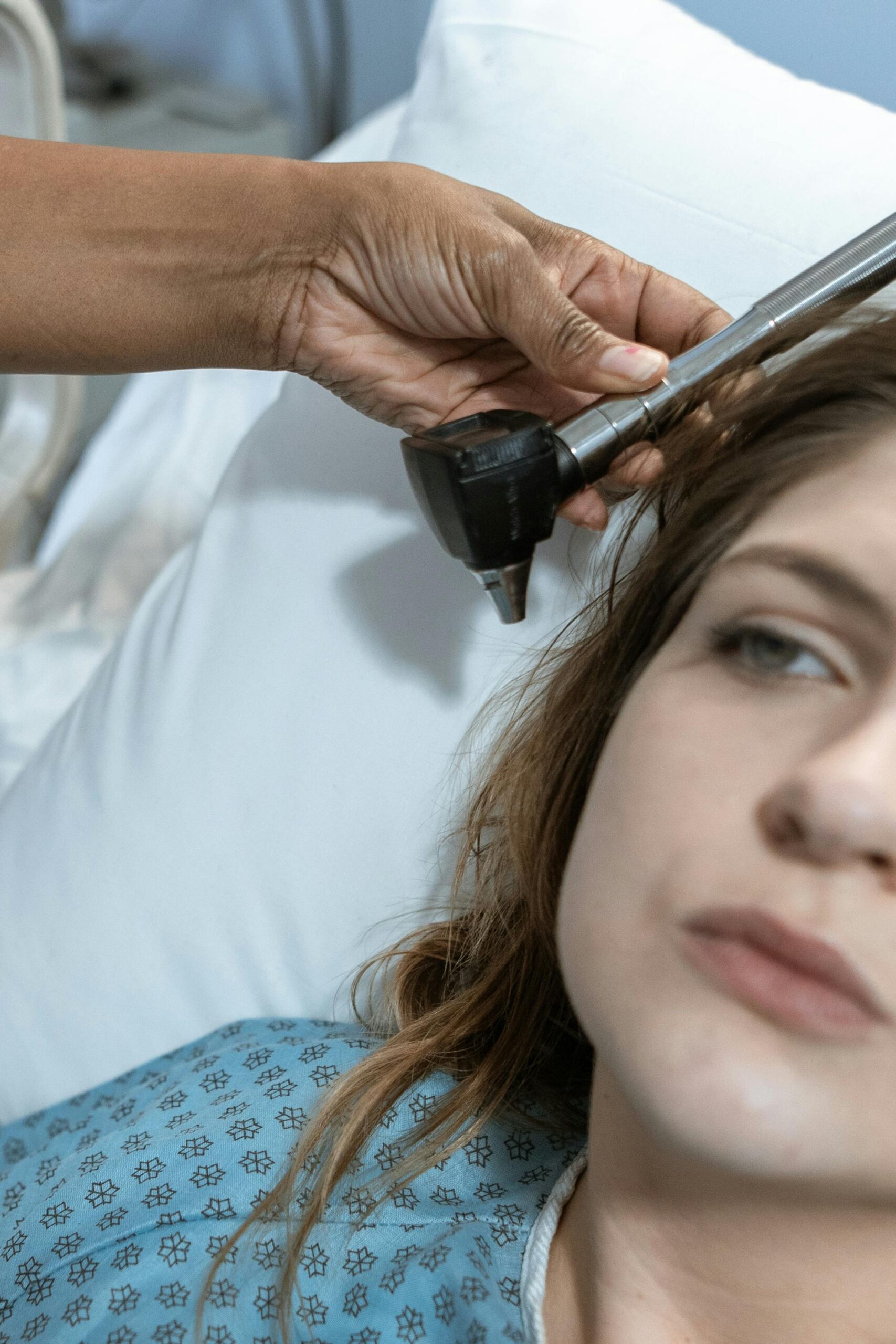 A nurse uses an ear thermometer to check the temperature of a resting female patient in a hospital setting.